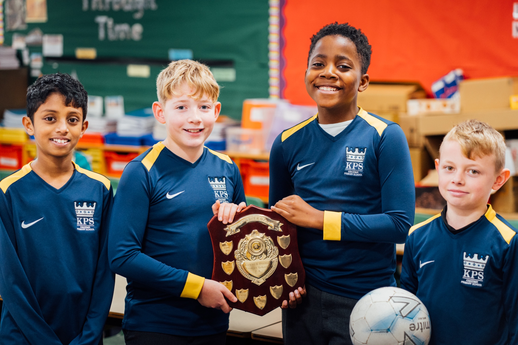 members of the school football team holding a trophy wearing their full kit